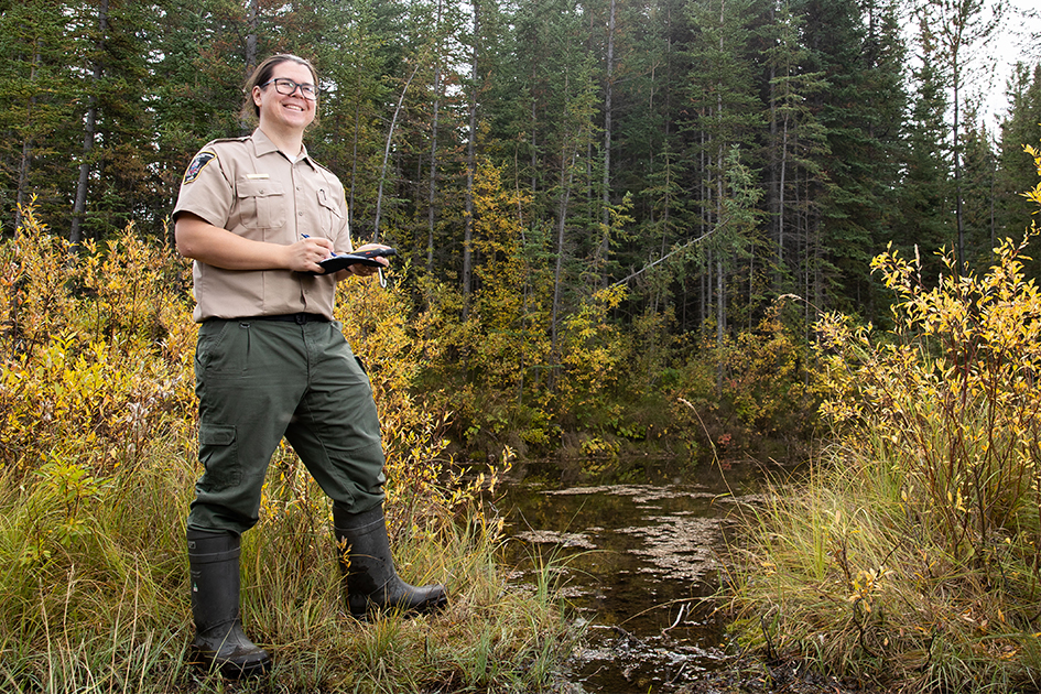 A natural resource officer standing near a water stream with his notebook.