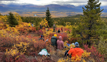 A group of hikers sitting on a mountainside overlooking a valley in the fall. 