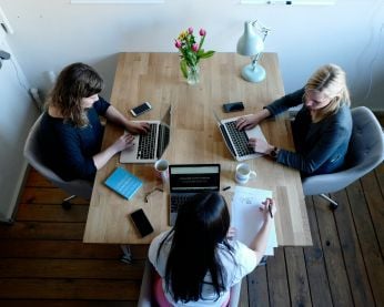 A photograph of three people sitting at a table working on their laptops.