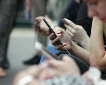 Personnes assises sur un banc en train de regarder leurs appareils mobiles.
