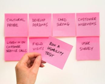 A whiteboard with pink post-it notes and a person holding 1 that reads usability testing