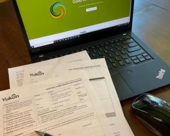 A  paper form overlaying a laptop displaying the digital service