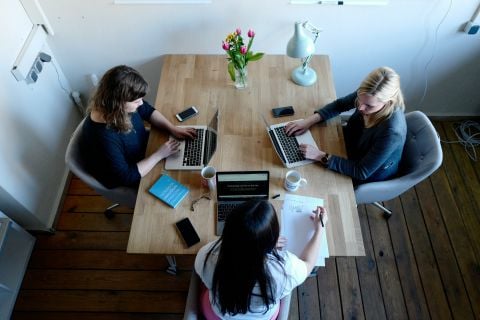A photograph of three people sitting at a table working on their laptops.
