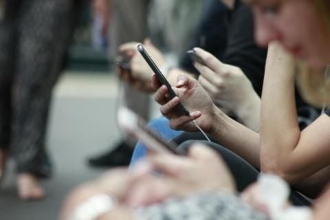 Personnes assises sur un banc en train de regarder leurs appareils mobiles.