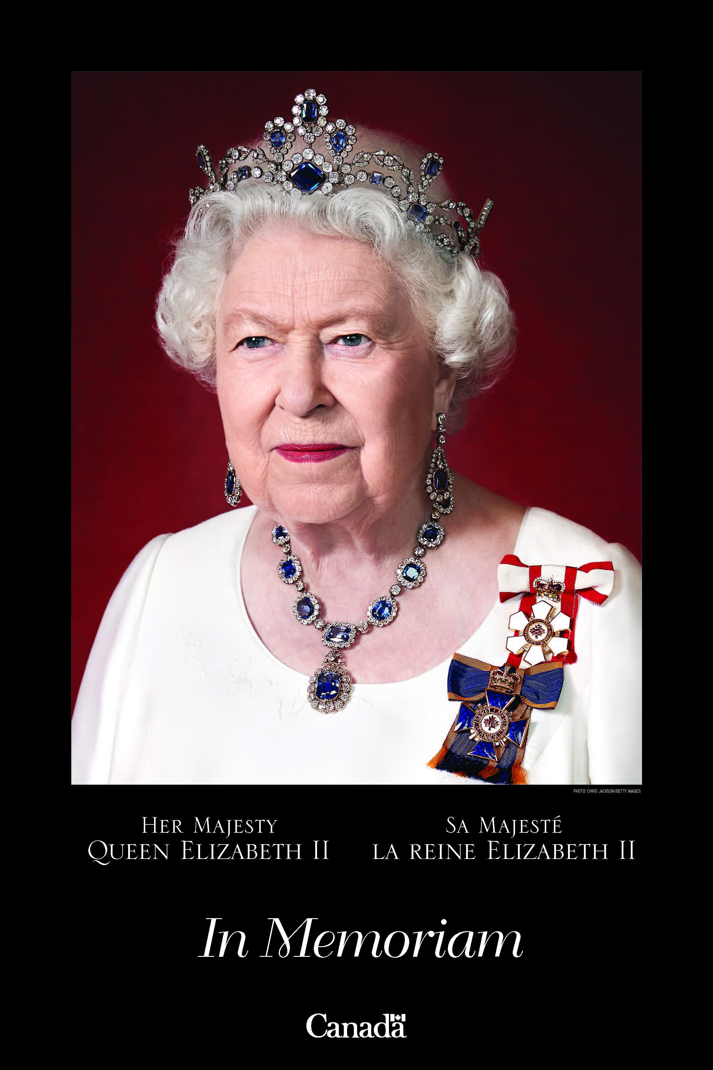 Her Majesty Queen Elizabeth II in a white dress and regalia against a dark red background.
