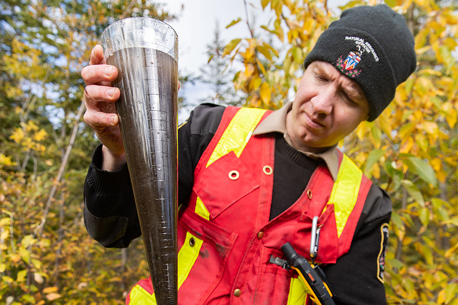 A natural resource officer looking at a cylinder full of muddy water.