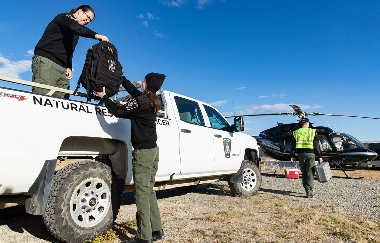 Natural resource officers offloading bags from a truck to load into a helicopter.