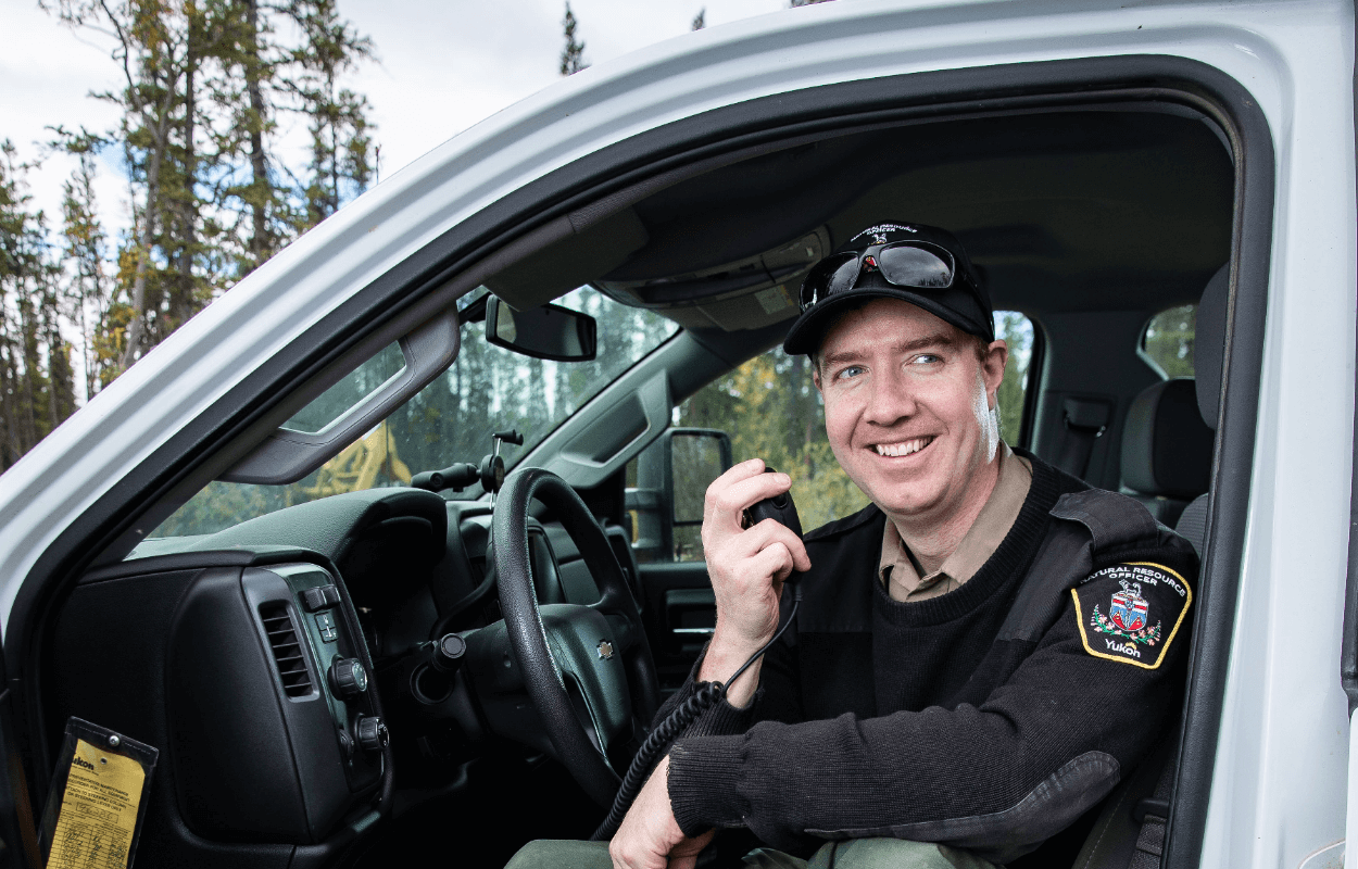 A natural resource officer sitting in his pick-up truck, smiling and holding a talkie-walkie.