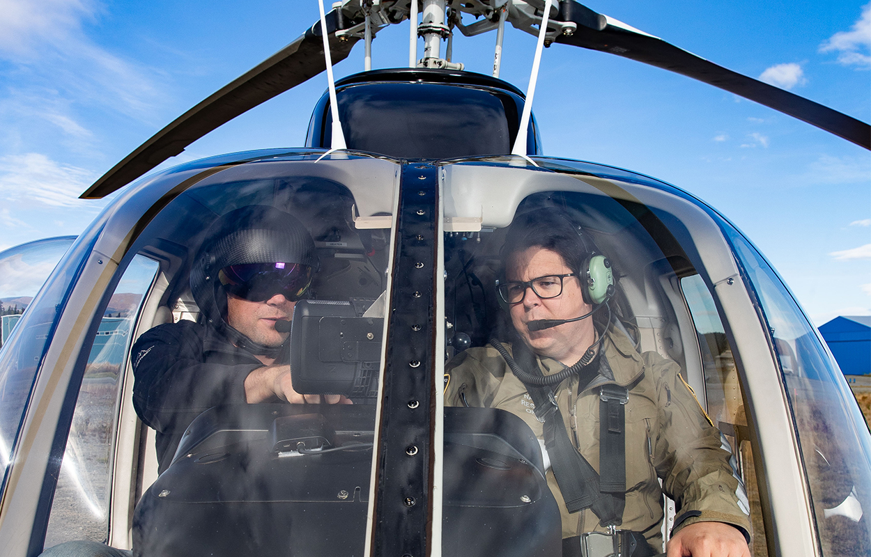 Two natural resource officers looking at a screen in a helicopter cockpit.