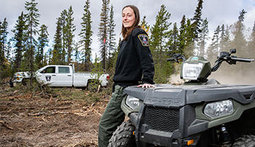 A natural resource officer leaning on an all-terrain vehicle in a field of cut trees.