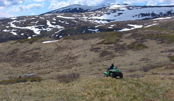An all-terrain vehicle cresting a hill in the mountains.