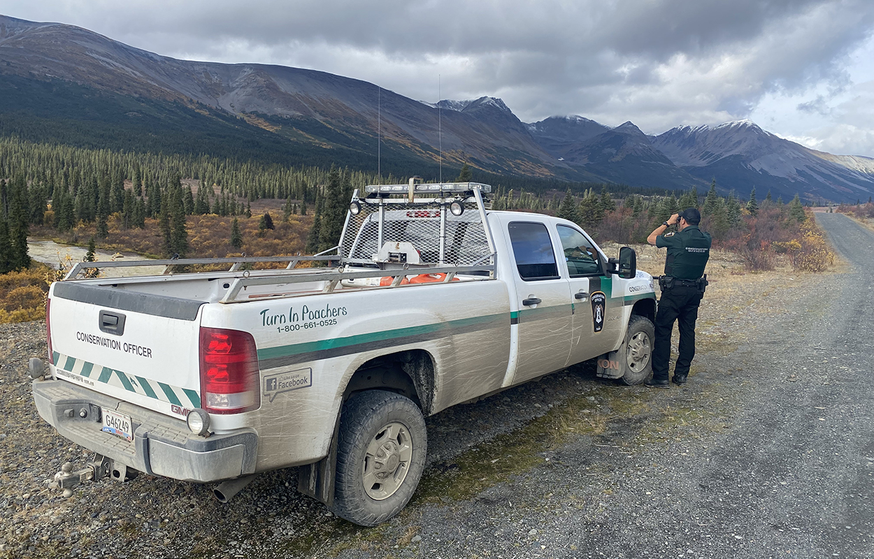 A conservation officer surveys the landscape beside his truck.
