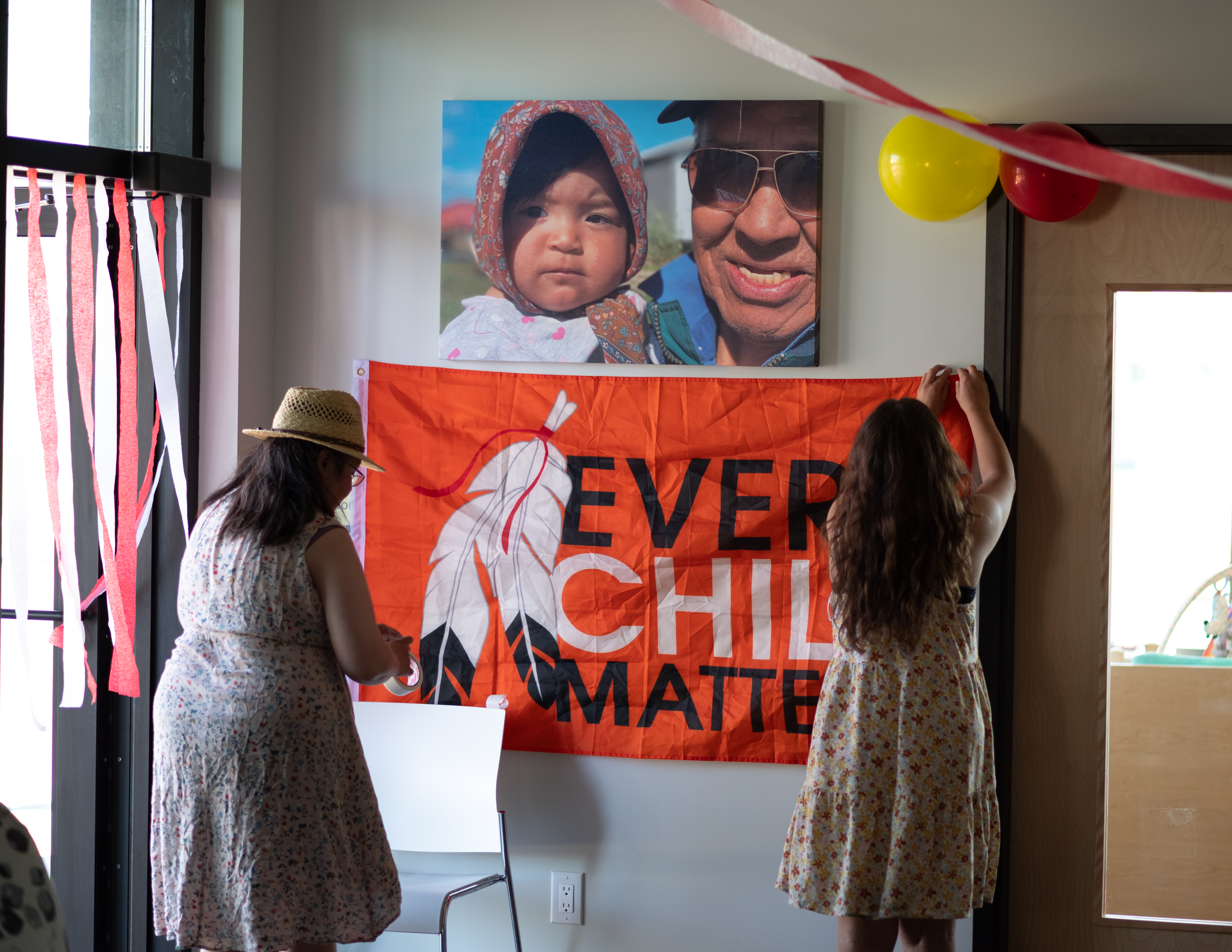 Two people hang an Every Child Matters flag at the opening of the new Yukon First Nation Education Directorate Early Years space in Whitehorse. 