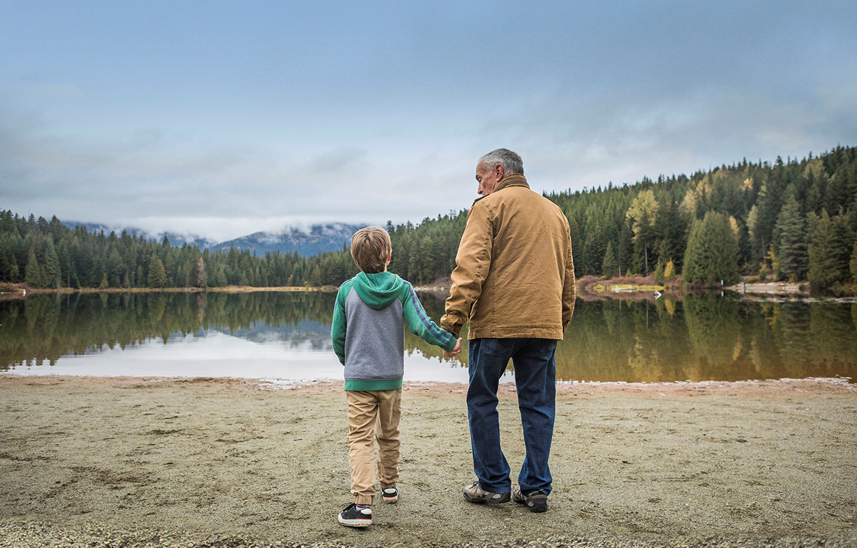 Older man and child walking toward a lake in the woods.