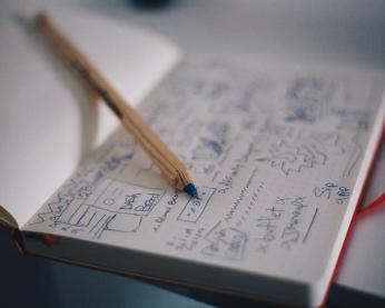 Close up of a pen laying across an open notebook filled with writing and sketches.