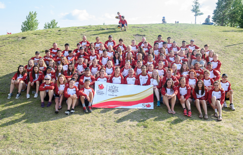 Image of Team Yukon contingent at 2017 Canada Summer Games. About 100 participants sit on a sunny hill. 